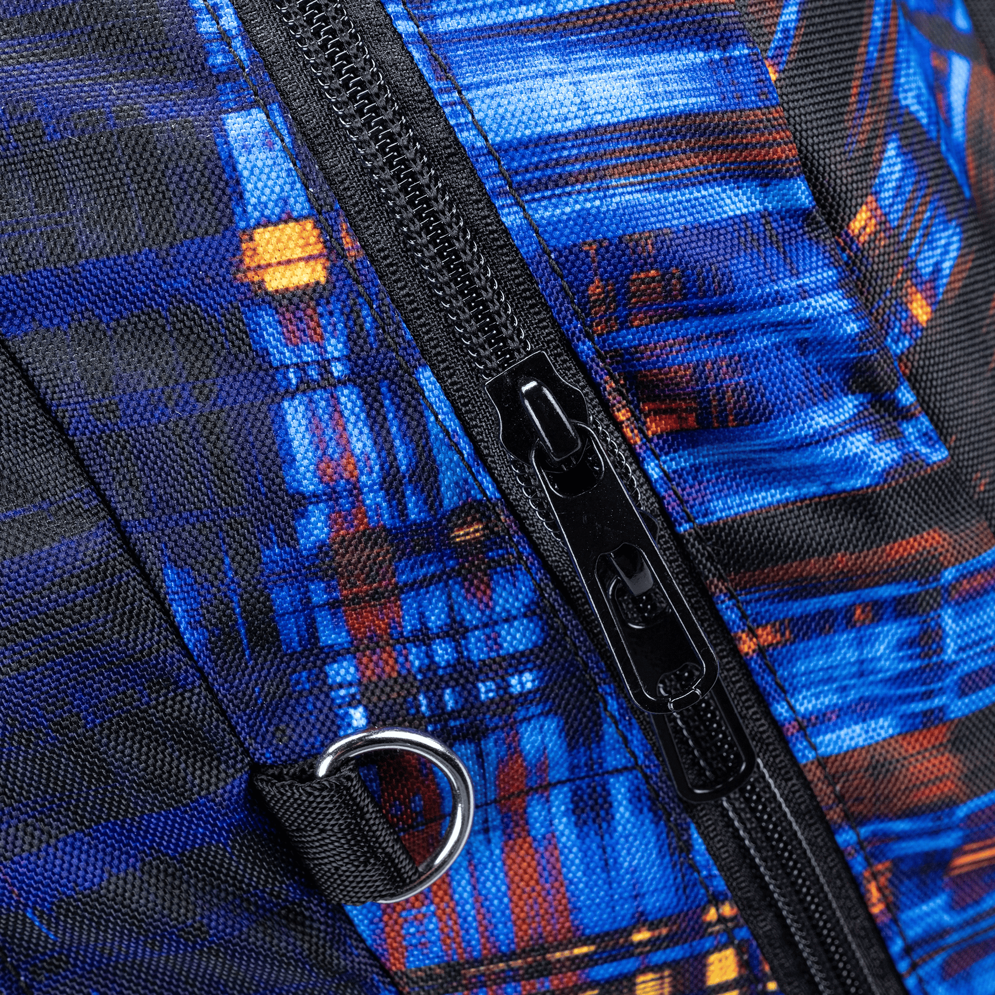 A close-up of a Totem School bag zip and D-ring on textured fabric in electric blue with orange accents.
