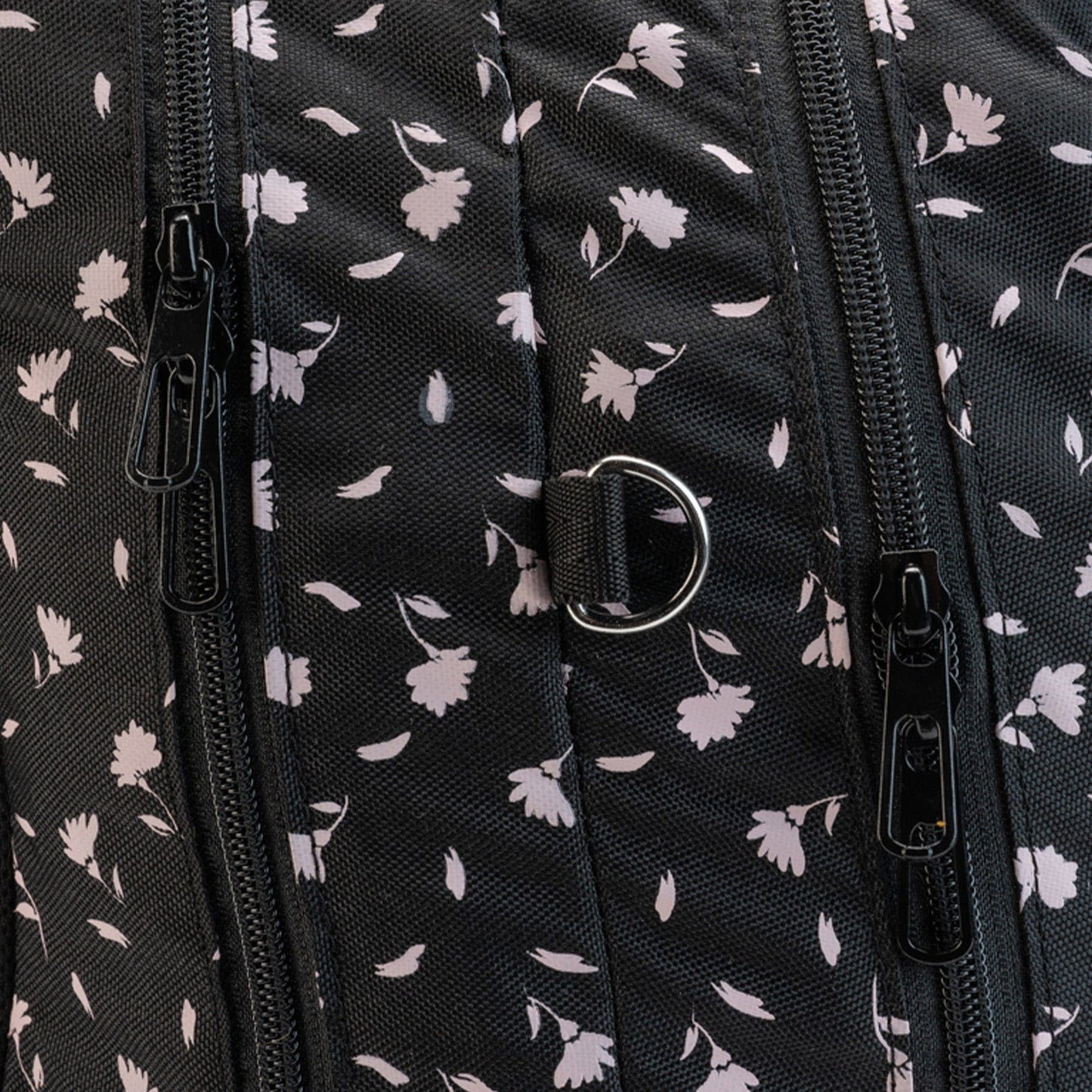 A closeup of black floral school bag fabric with zippers and a small metal D-ring attachment.