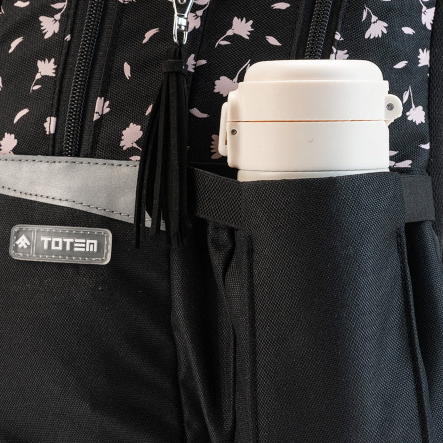 A close-up of a black Totem school bag side pocket holding a white insulated bottle.