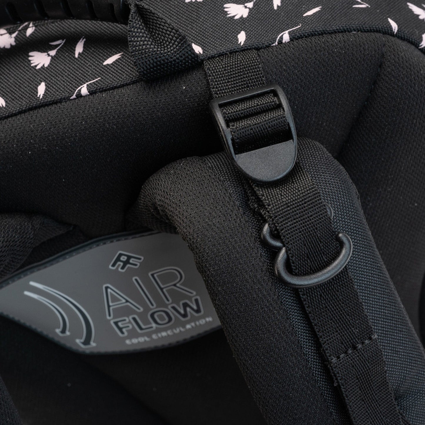 A closeup of a padded shoulder strap of the black floral backpack, featuring an adjustable strap with a plastic buckle.